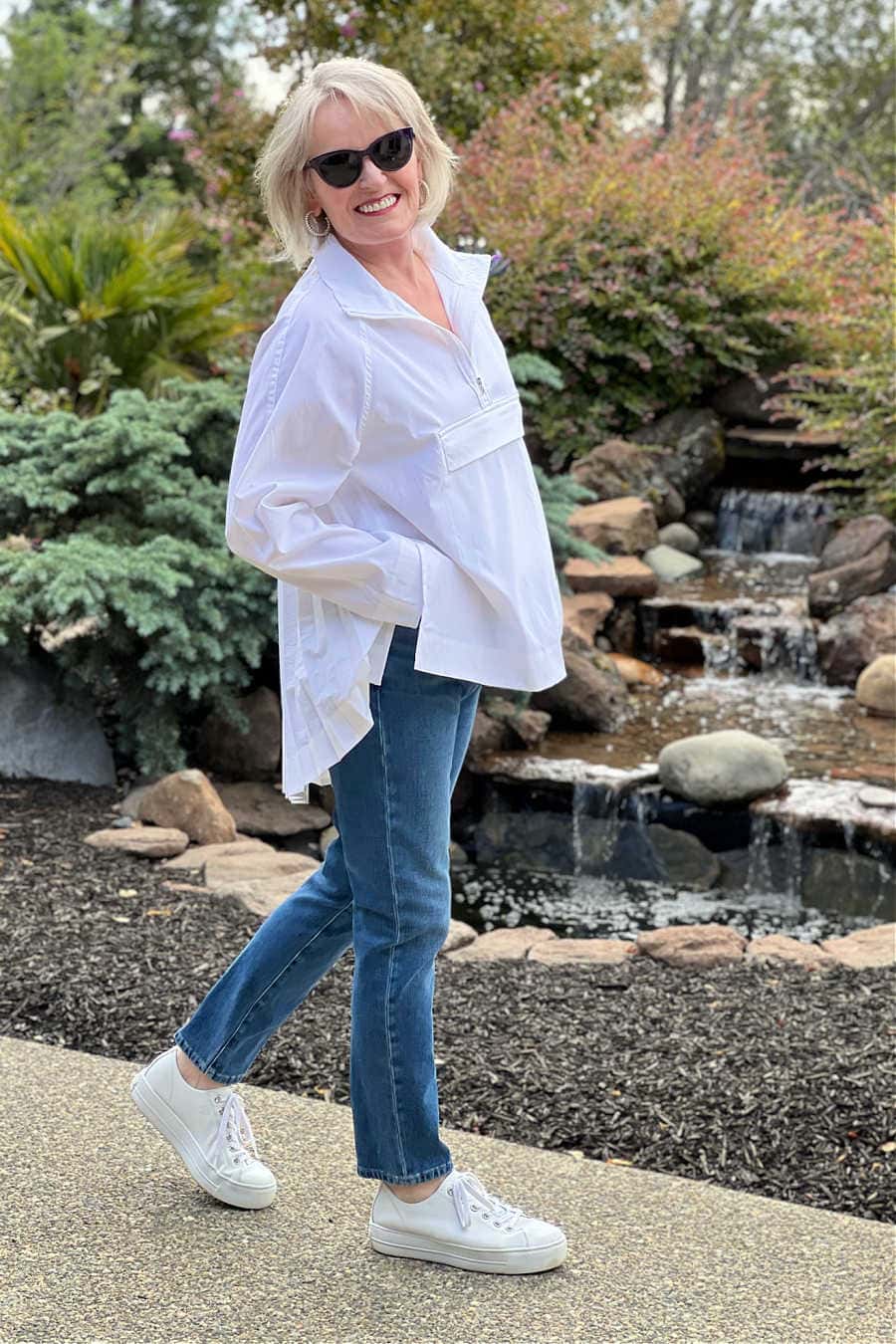 Woman wearing athleta sojourn top with blue jeans and white sneakers