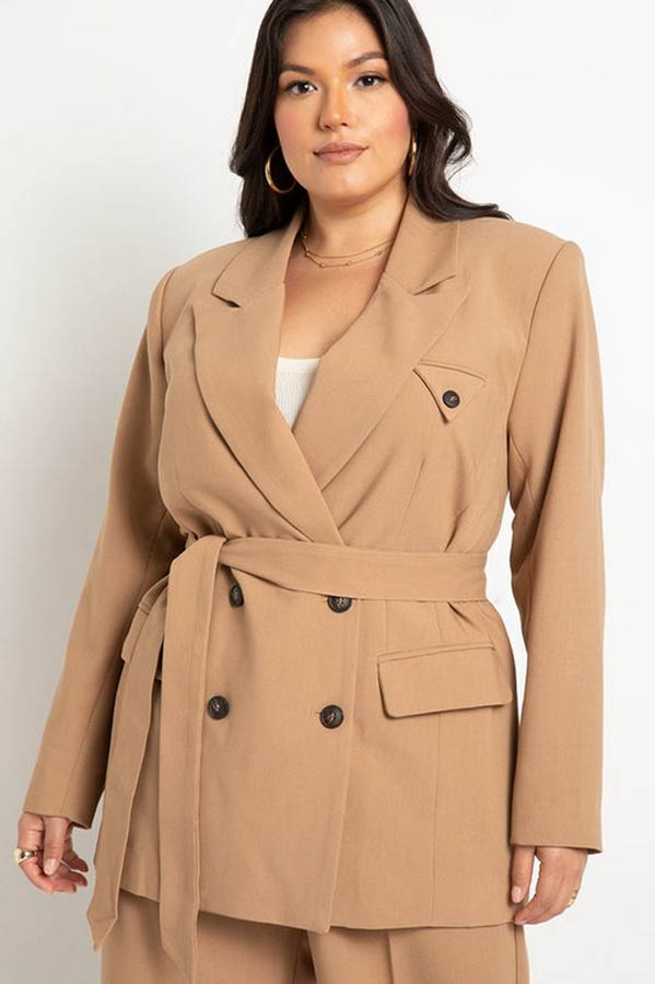 The model wears a tan plus-size blazer, a must-have for fall fashion.