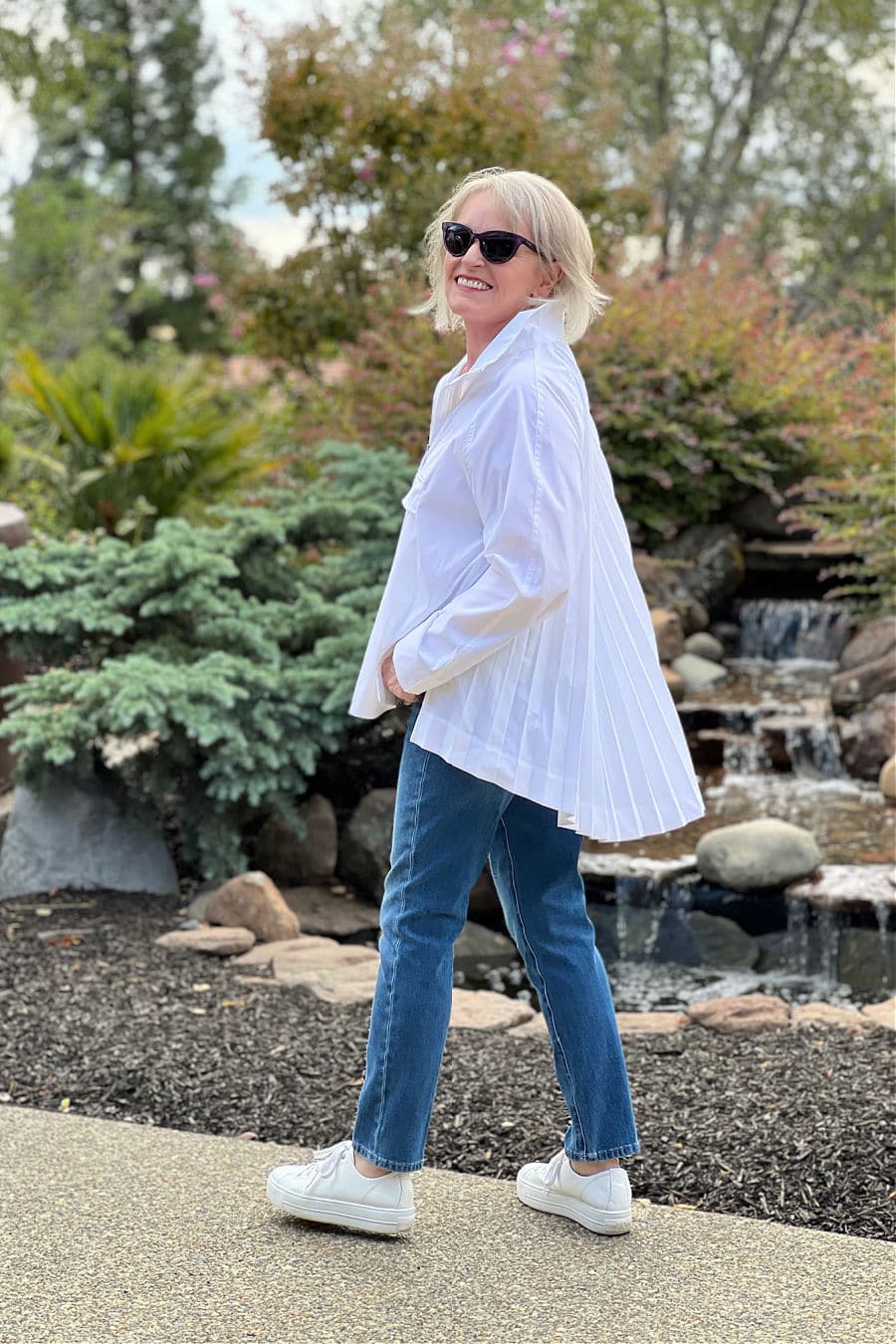 Over 50 blogger Jennifer Connolly in front of a fountain in a white shirt and blue jeans by Acerta Sojourn
