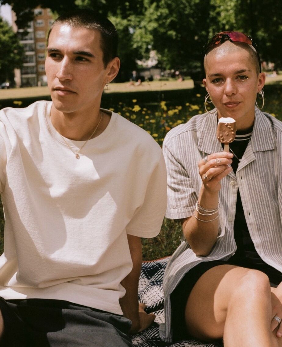 A man and a woman are sitting in a park and holding an ice cream bar that the woman has partially eaten.